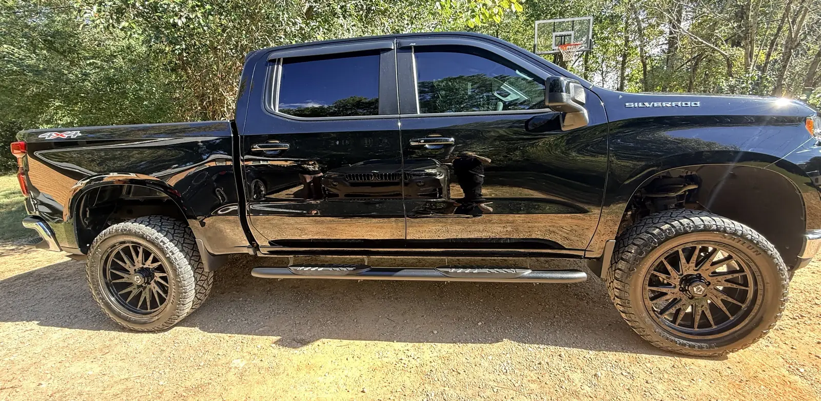 Black Chevrolet Silverado with a deep gloss finish reflecting the trees